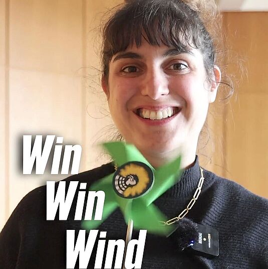 Foto von Marie Kollenrott mit einem Windrad mit dem grünen Fraktionslogo. Text: "Win Win Wind"